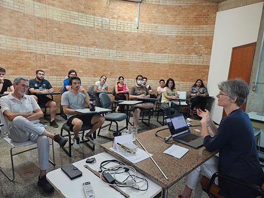 woman with glasses sitting, speaking to group of people